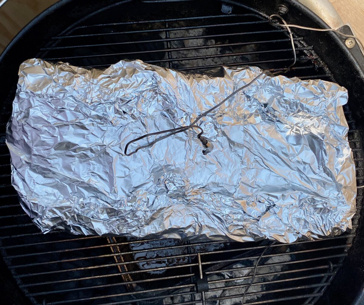 Wrapped smoked brisket positioned on the charcoal grill to complete the cook process.