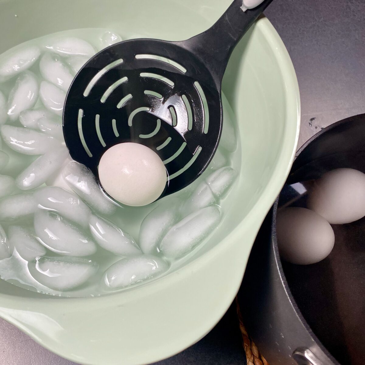 Top view of a hard boiled egg being lowered into an ice bath to stop the cooking process.