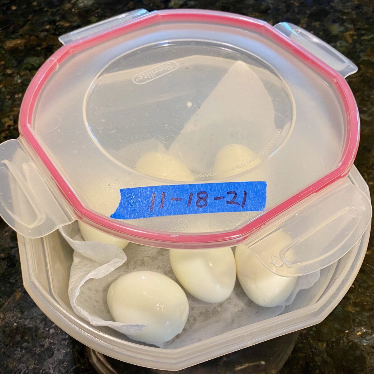 6 peeled boiled eggs in plastic container with damp paper towel. The lid has a piece of tape showing the boil date.