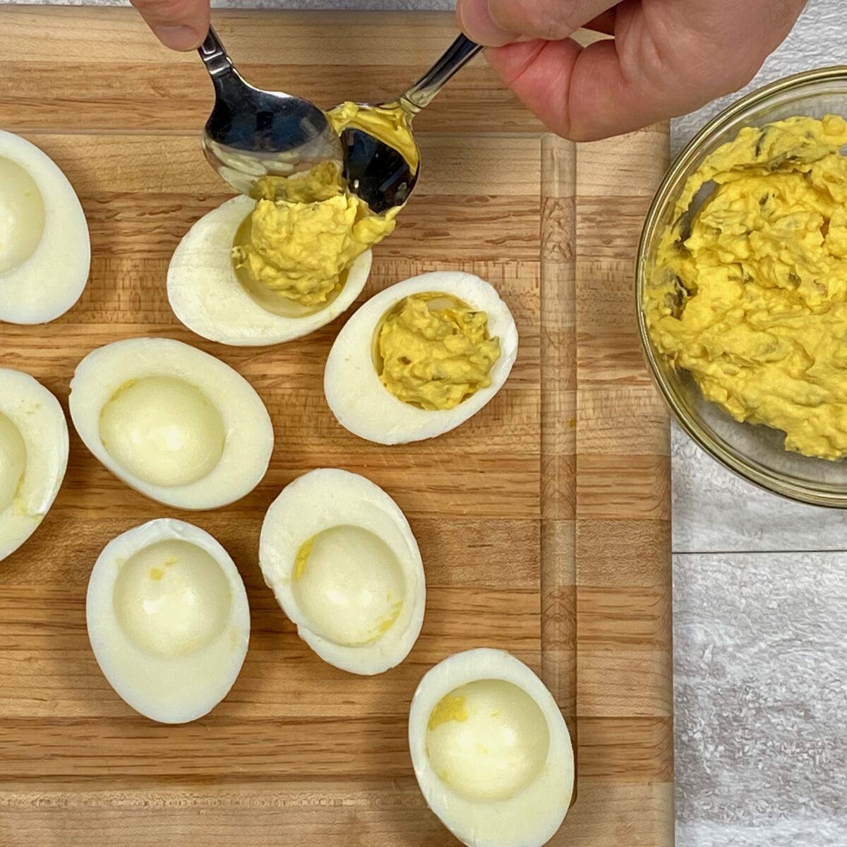 Overhead view showing how to use two spoons to fill a hard boiled egg white with the deviled egg mixture.