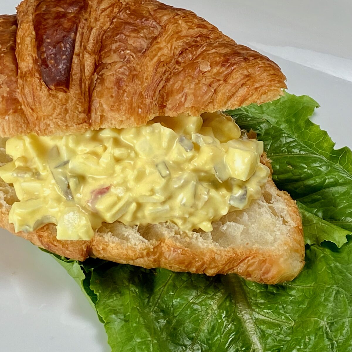 Egg salad with relish on a croissant, served on a bed of lettuce.