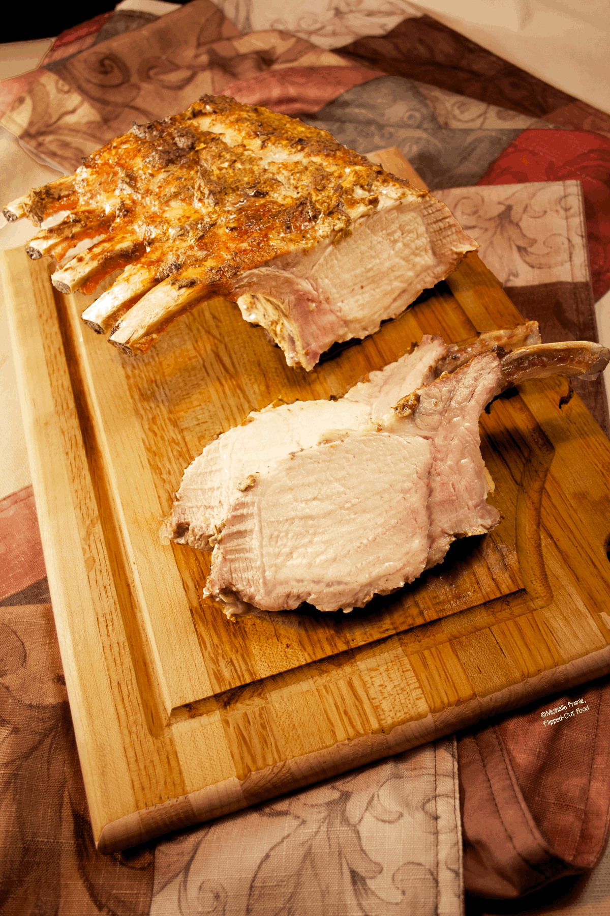 Side view of a whole rack of pork with two chops sliced off of it on a cutting board.