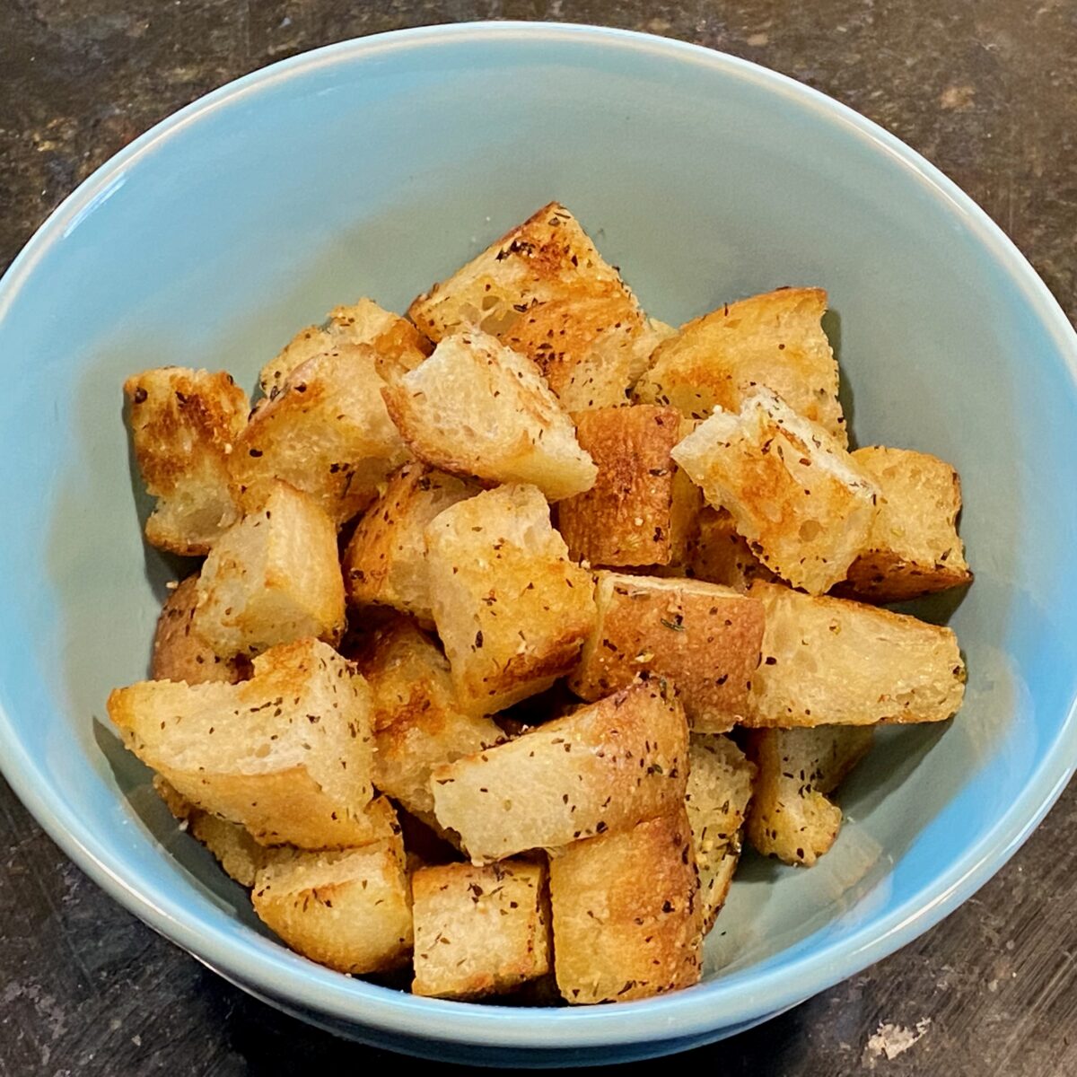 Overhead view of freshly made stovetop croutons in a blue bowl.