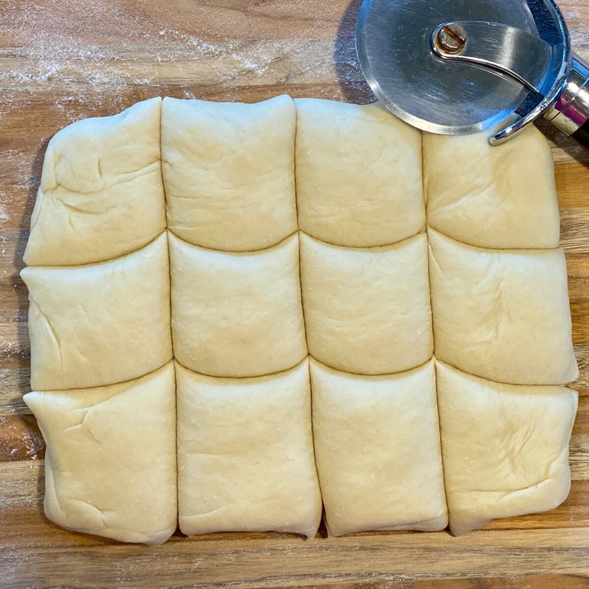 The risen dough, formed into a rectangle, and then cut into 12 roughly equal pieces with a pizza cutter.