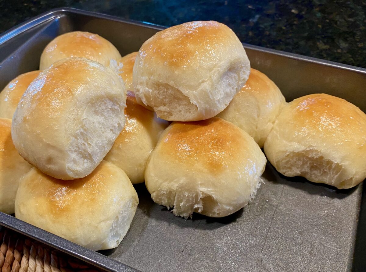 Side view of a batch of easy dinner rolls, fresh from the oven. I've pulled a couple of the rolls out of the pan and set them on top so you can see the incredible crumb.