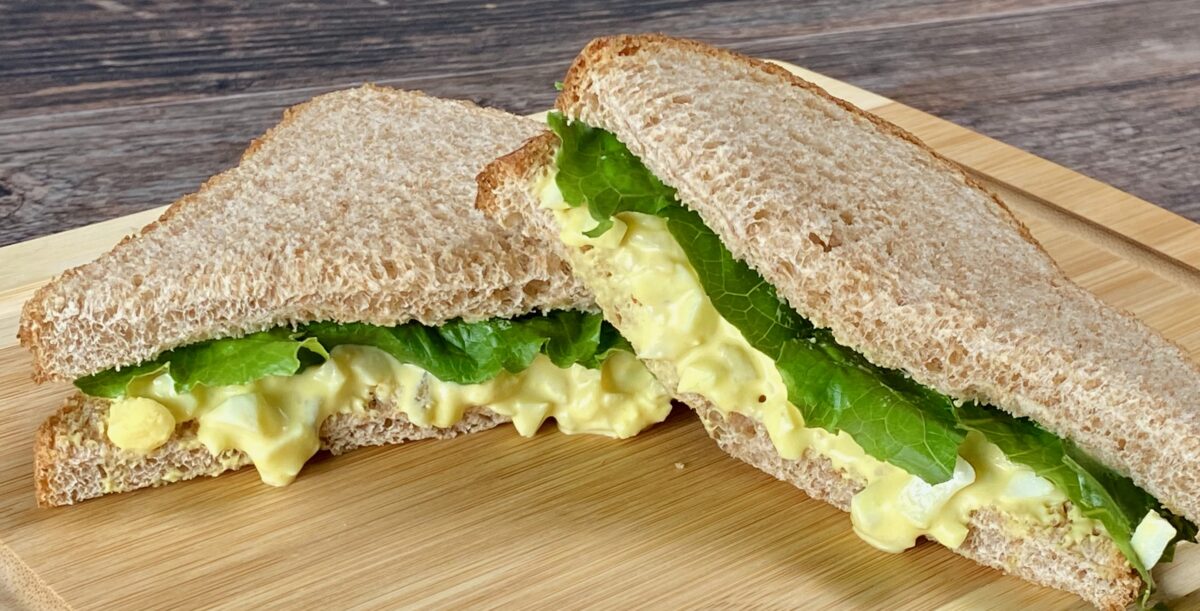 Egg salad on wheat bread with lettuce on a wooden cutting board.