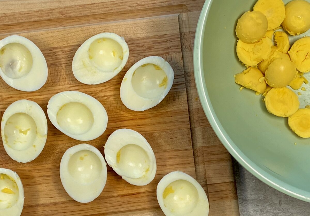 Overhead view of hard boiled eggs that have been cut in half with their yolks removed and placed in adjacent bowl. 