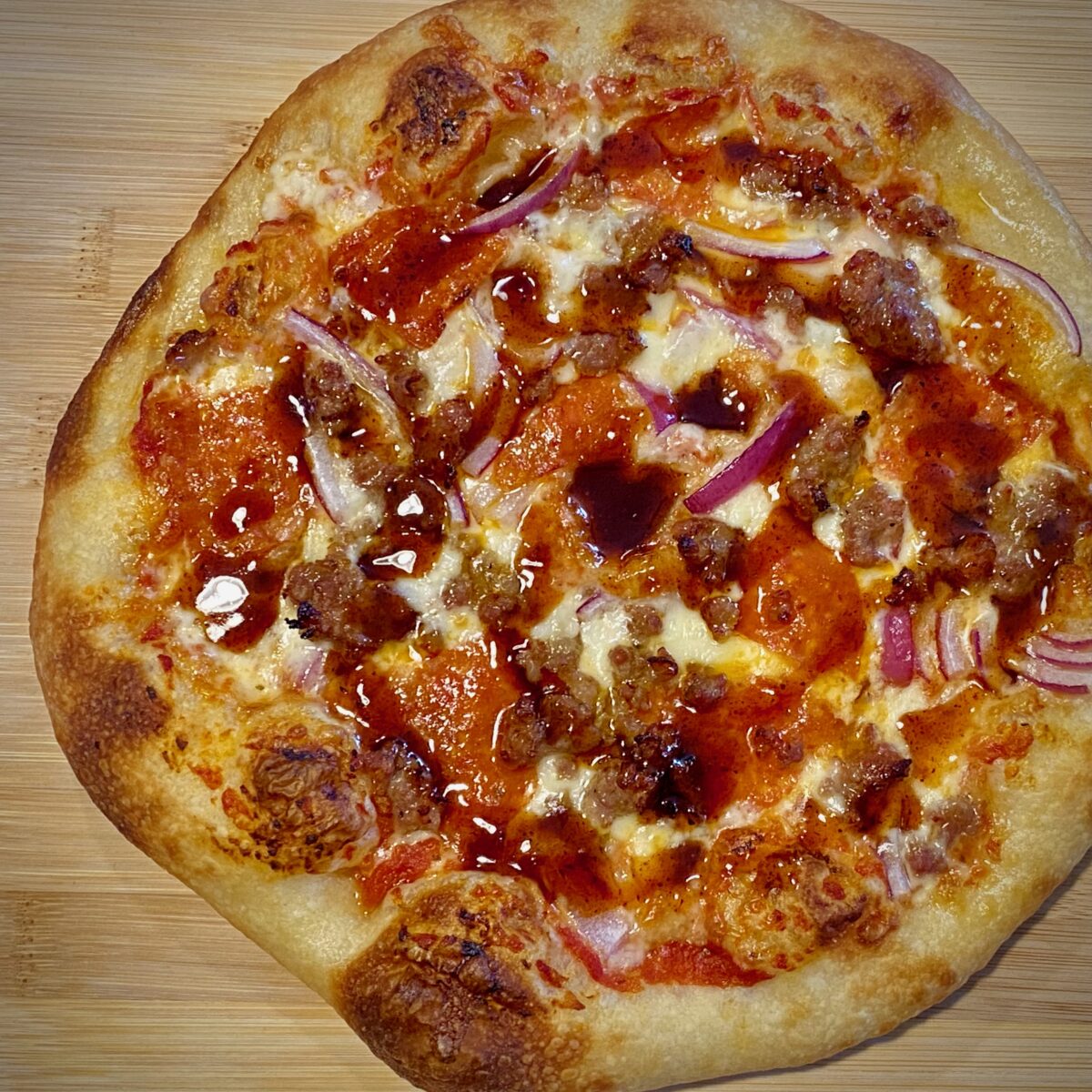 top view of sausage, pepperoni and red onion pizza that has been topped with a swirl of barbeque sauce.