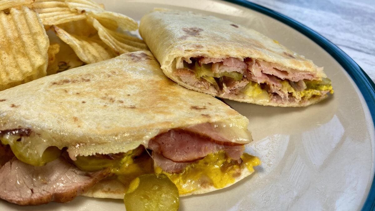 Side view of a cuban quesadilla on a plate with potato chips.