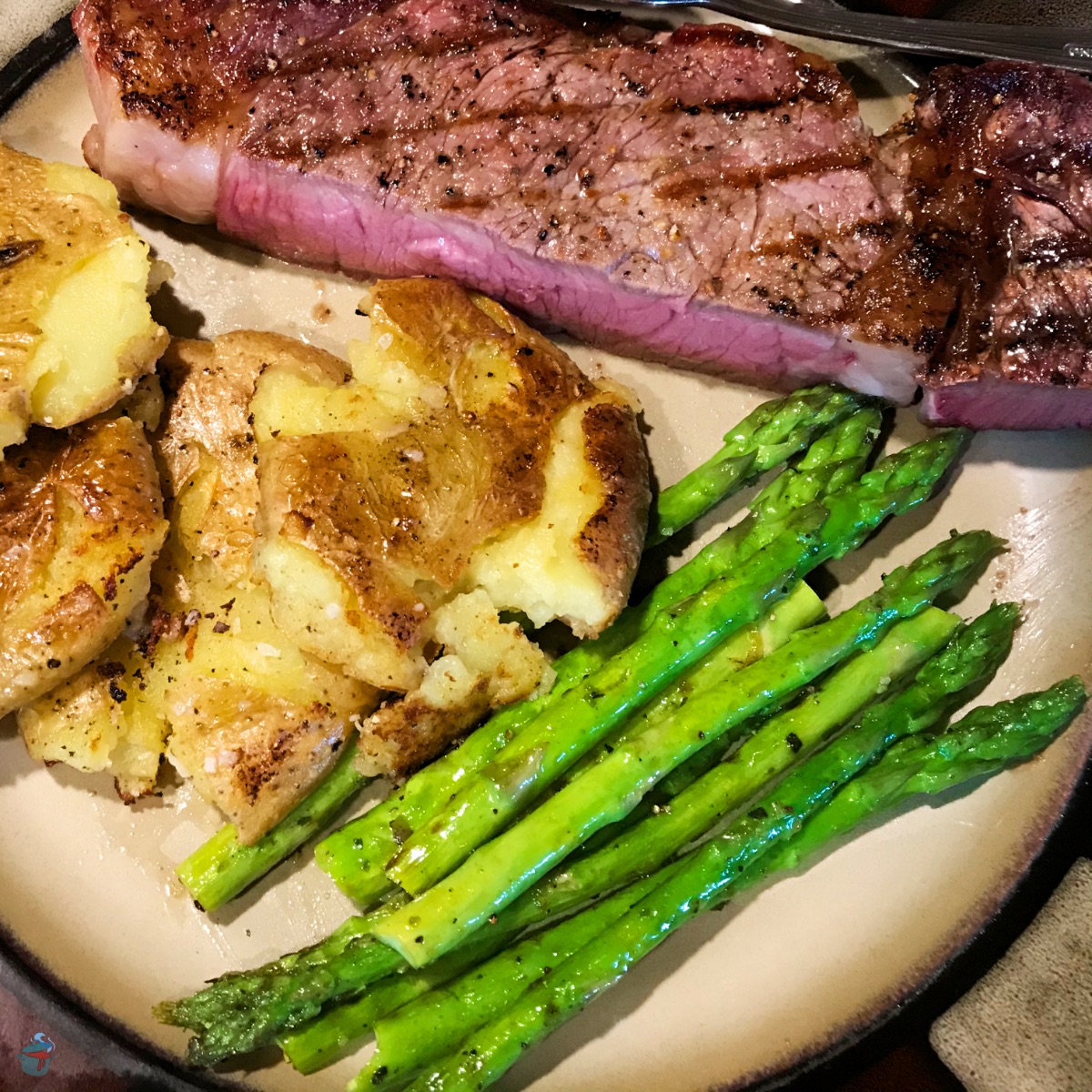 Microwave Asparagus served on a plate with a half of a New York Strip Steak and rosemary smashed potatoes.