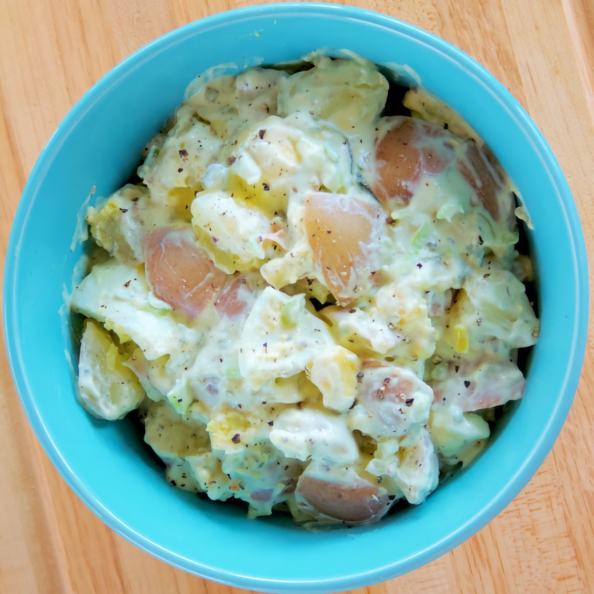 Classic Potato Salad in a blue serving bowl set atop a light wooden cutting board.