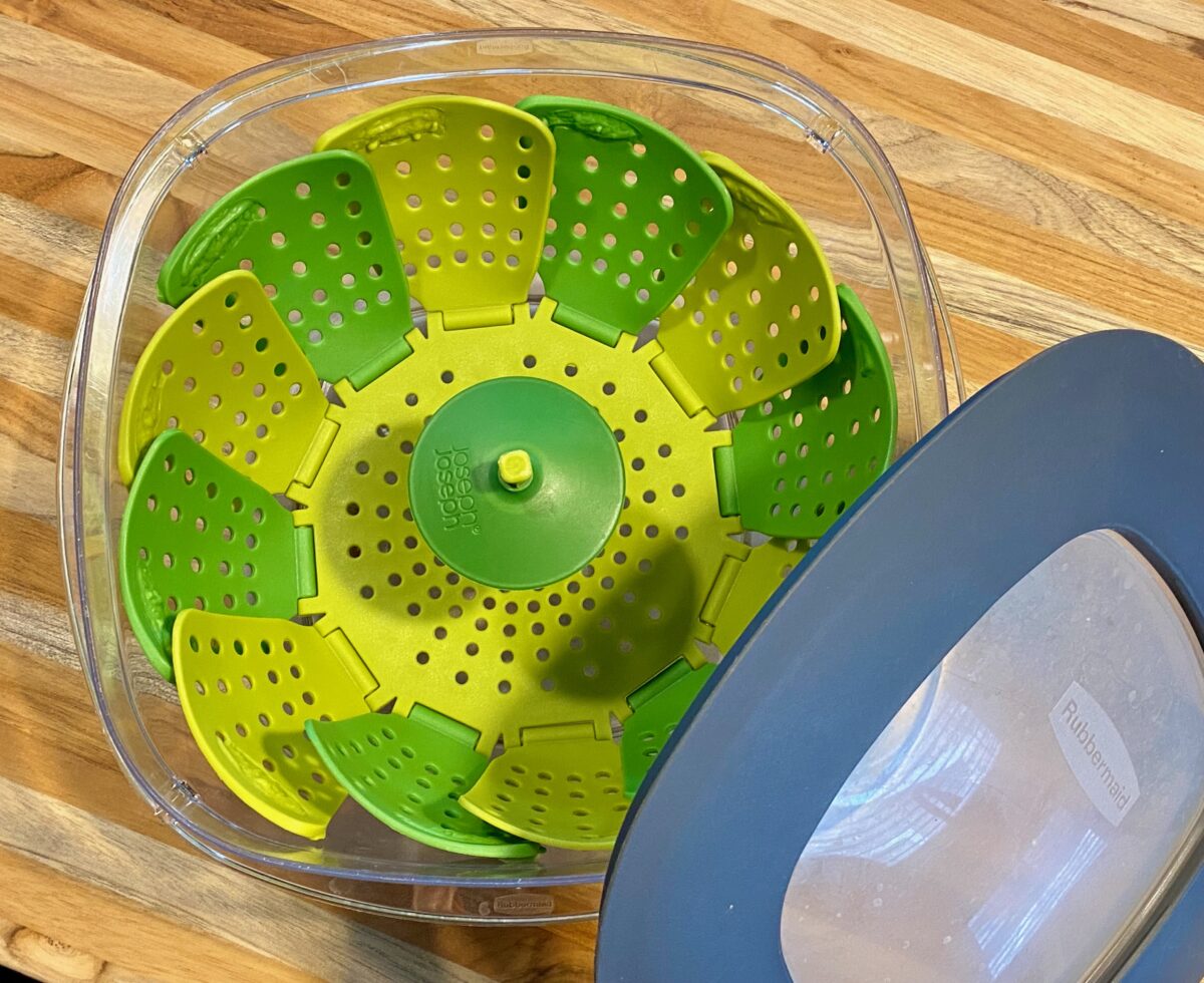 Top view of homemade vegetable steamer which consists of a microwaveable rubber colander inside a large plastic container that has a lid.