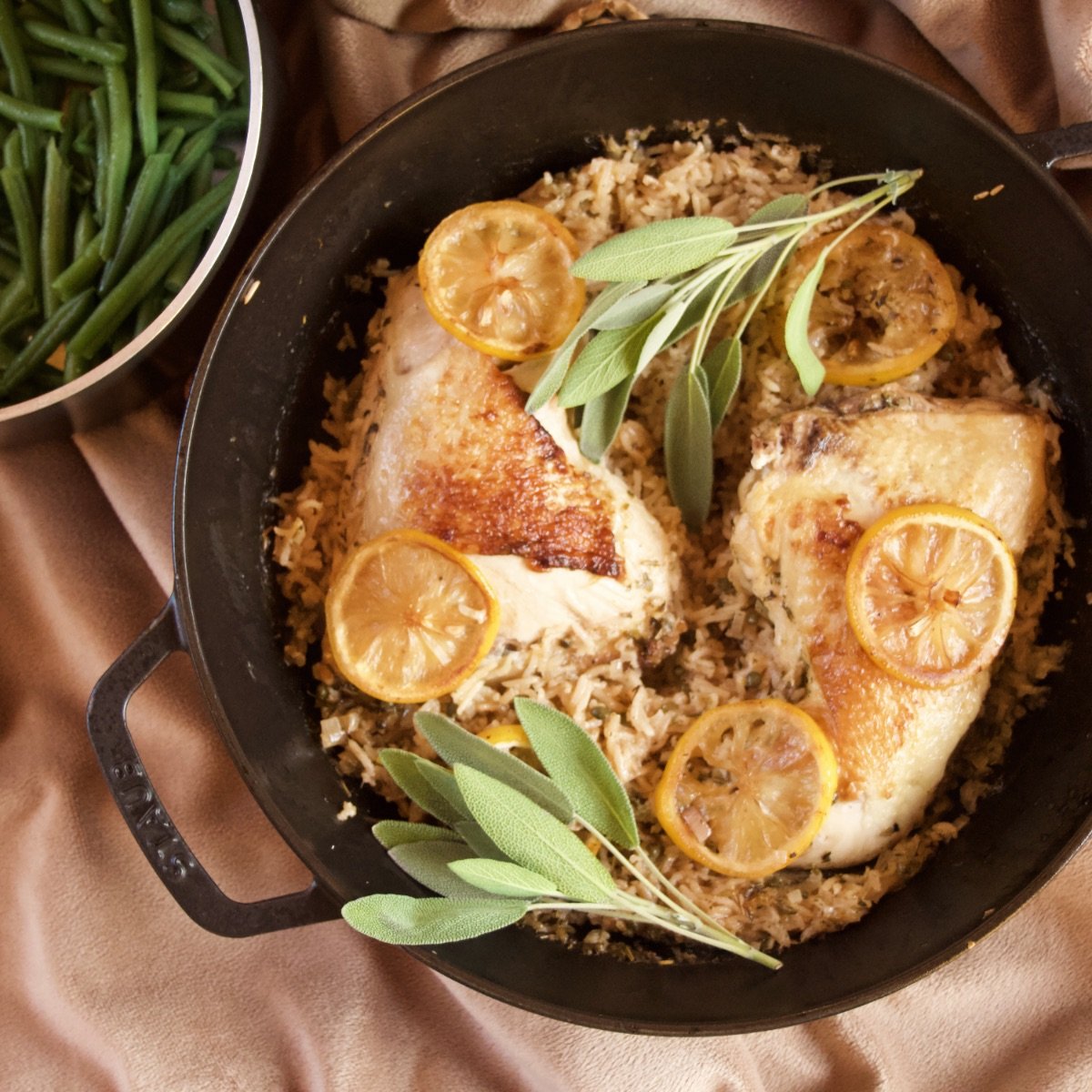 One-Pan Meyer Lemon Chicken with Rice, fresh from the oven, garnished with sage and sitting next to a pan of steamed green beans.