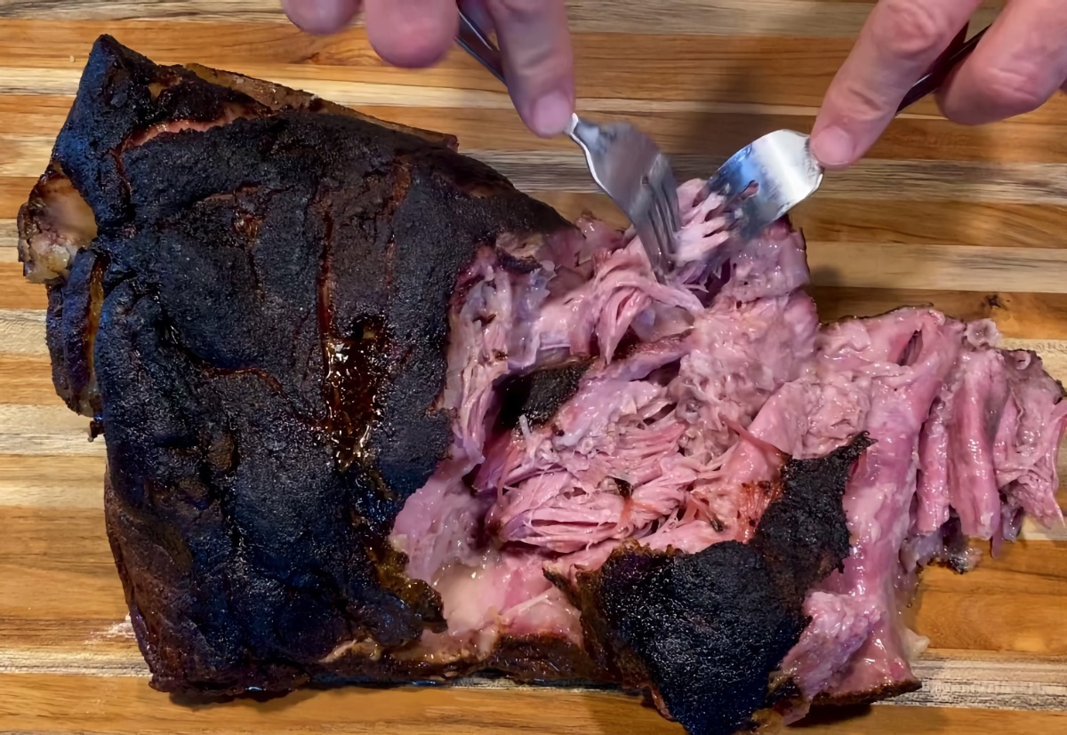 Pulling the smoked pork butt using two forks, following the resting period.