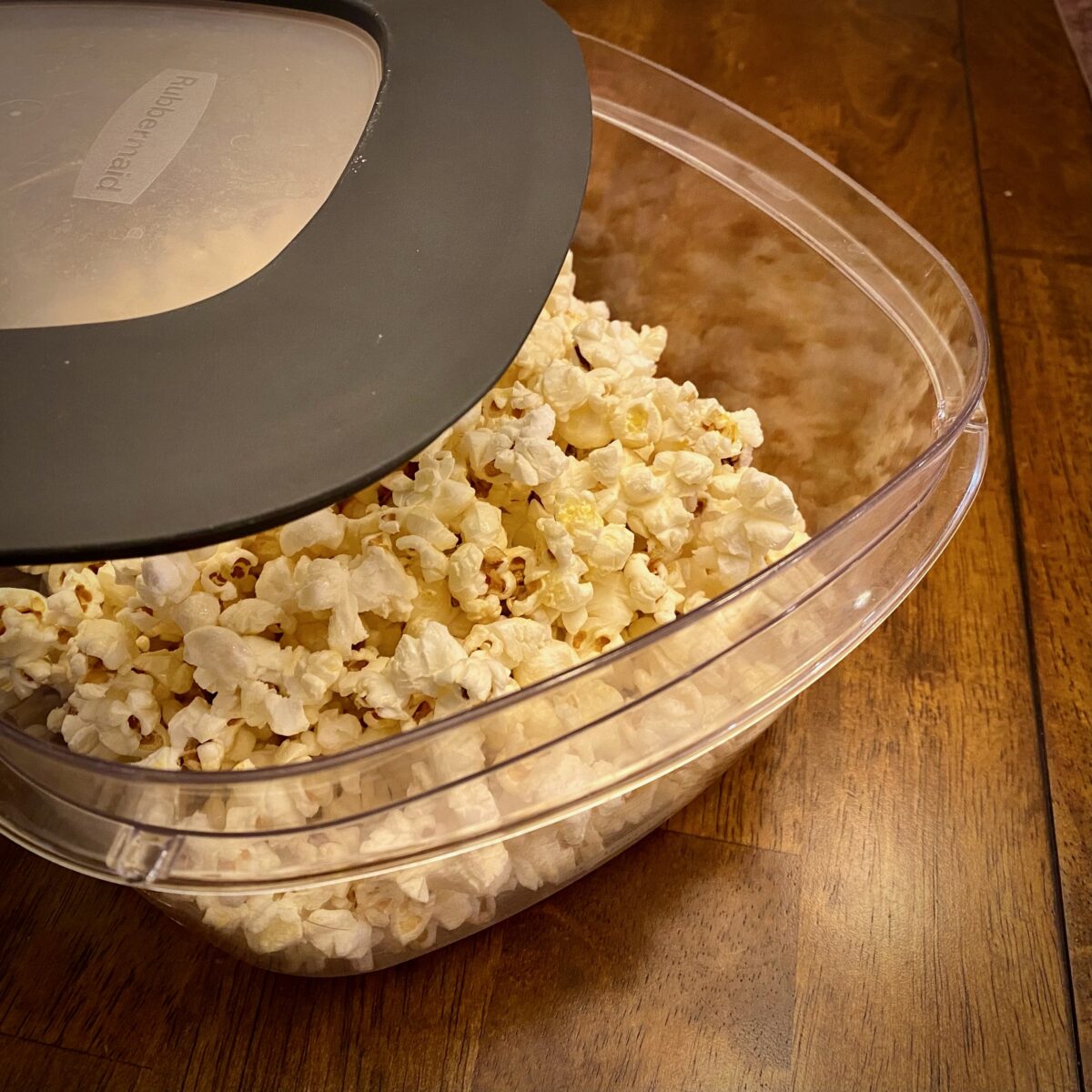 Kettle corn inside large tupperware container with lid partially closed.