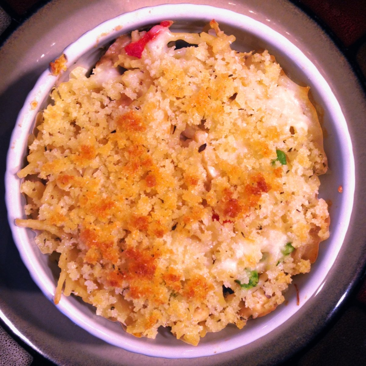 An individual serving of One-Pot Turkey Tetrazzini in a white ramekin. The serving is topped with buttery bread crumbs that have been browned under the broiler. 