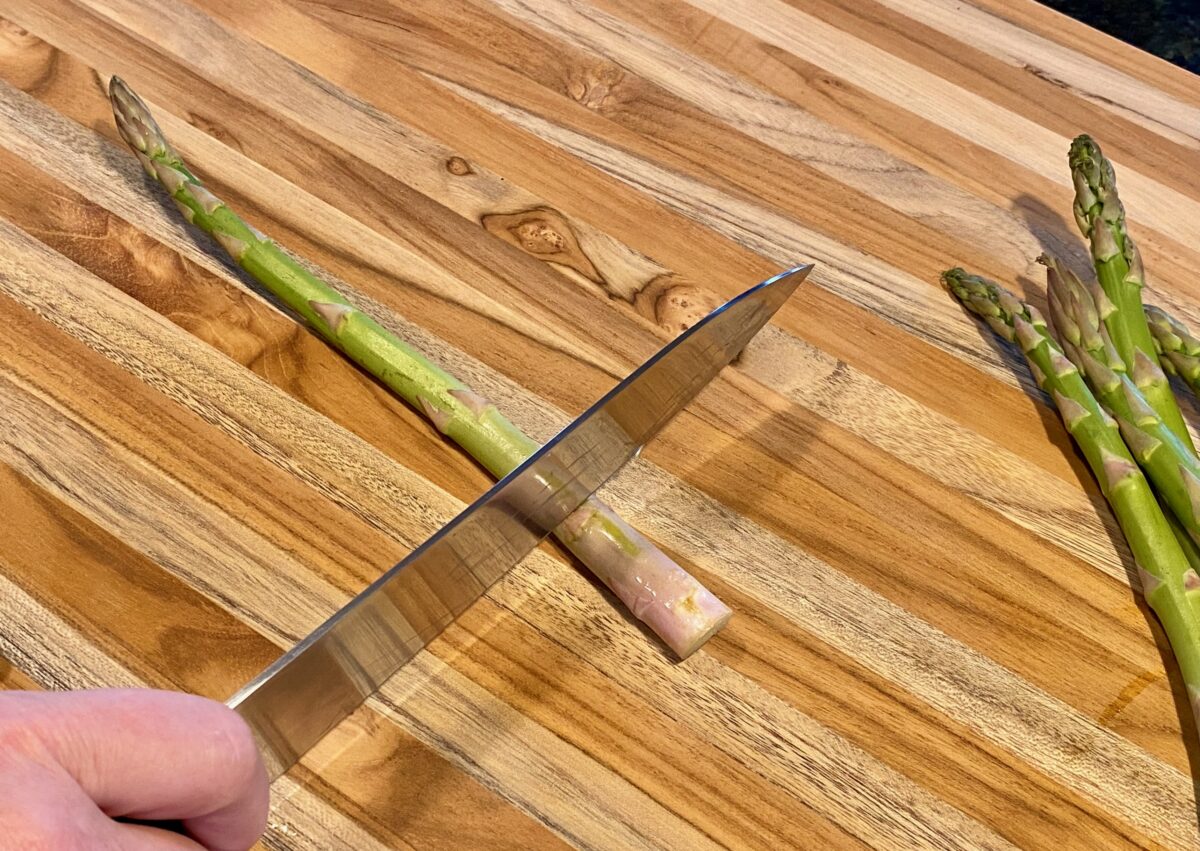 Top view of a knife at the proper position on where to trim the woody asparagus ends.