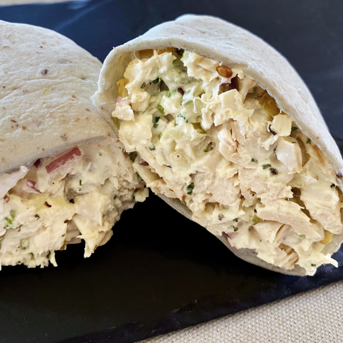 Close up view of a wrap of chicken salad with relish that has been cut in half. A view of the inside both halves of the wrap is shown.