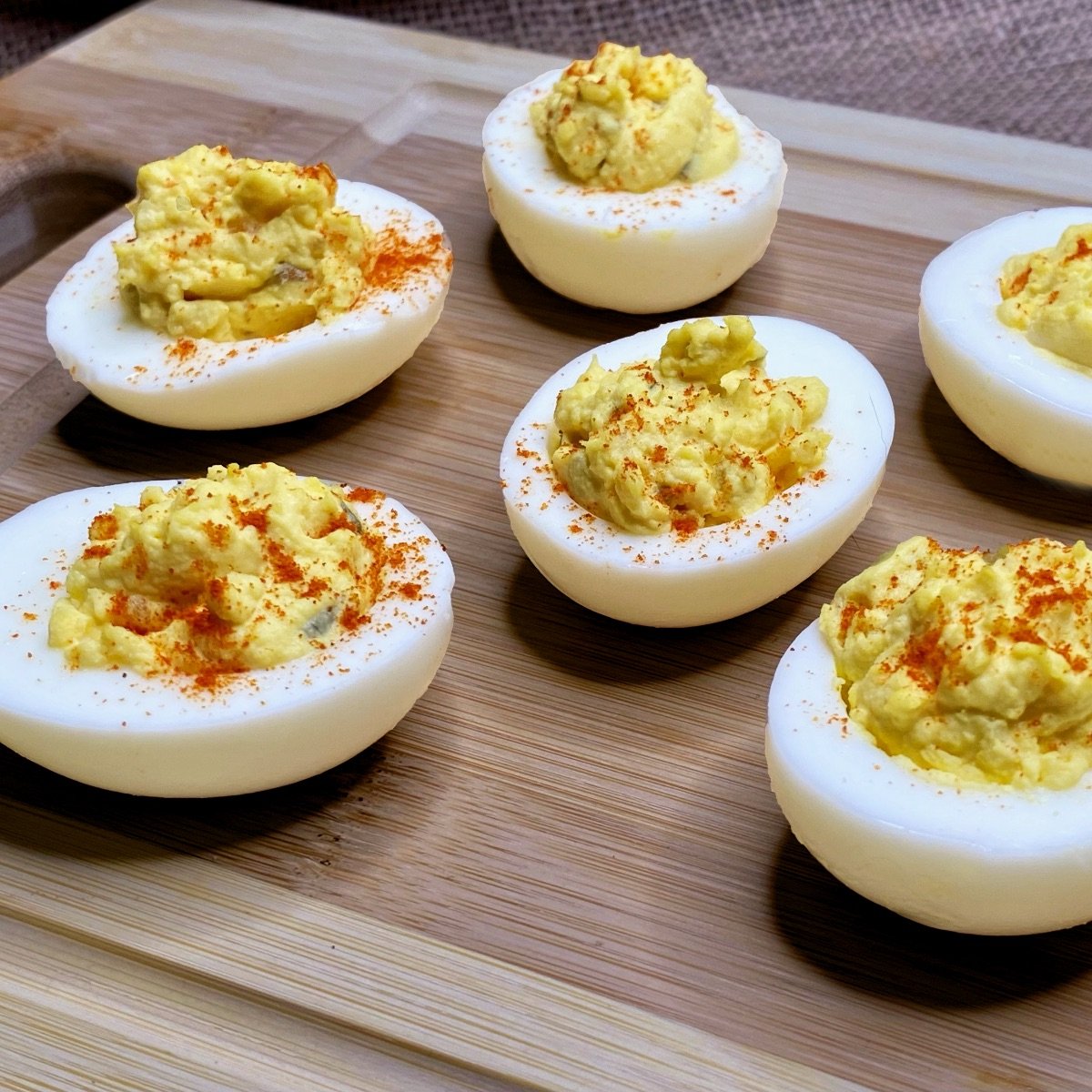 A close-up side view of Deviled Eggs with Relish on a wooden cutting board, sprinkled with paprika.