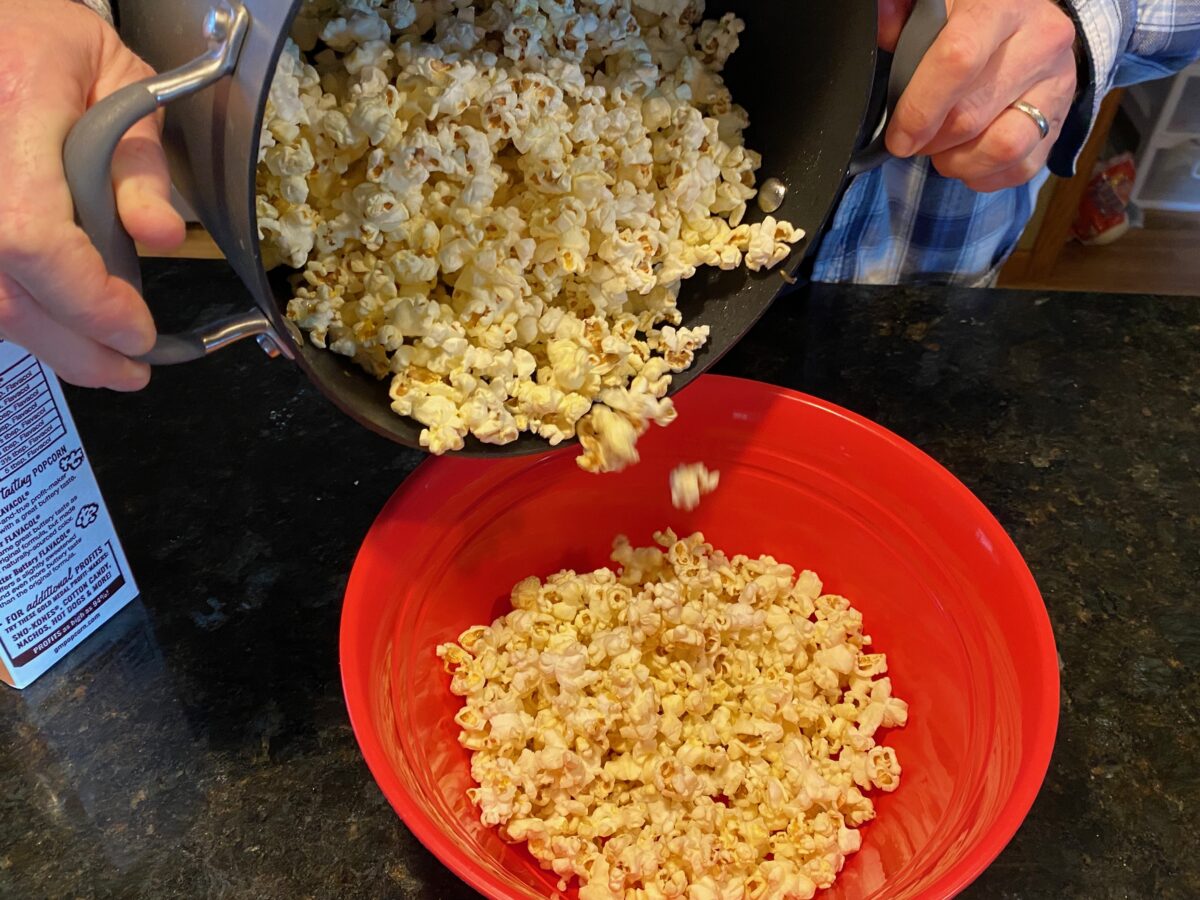 Pouring Movie Theater Popcorn into a large red bowl for serving.