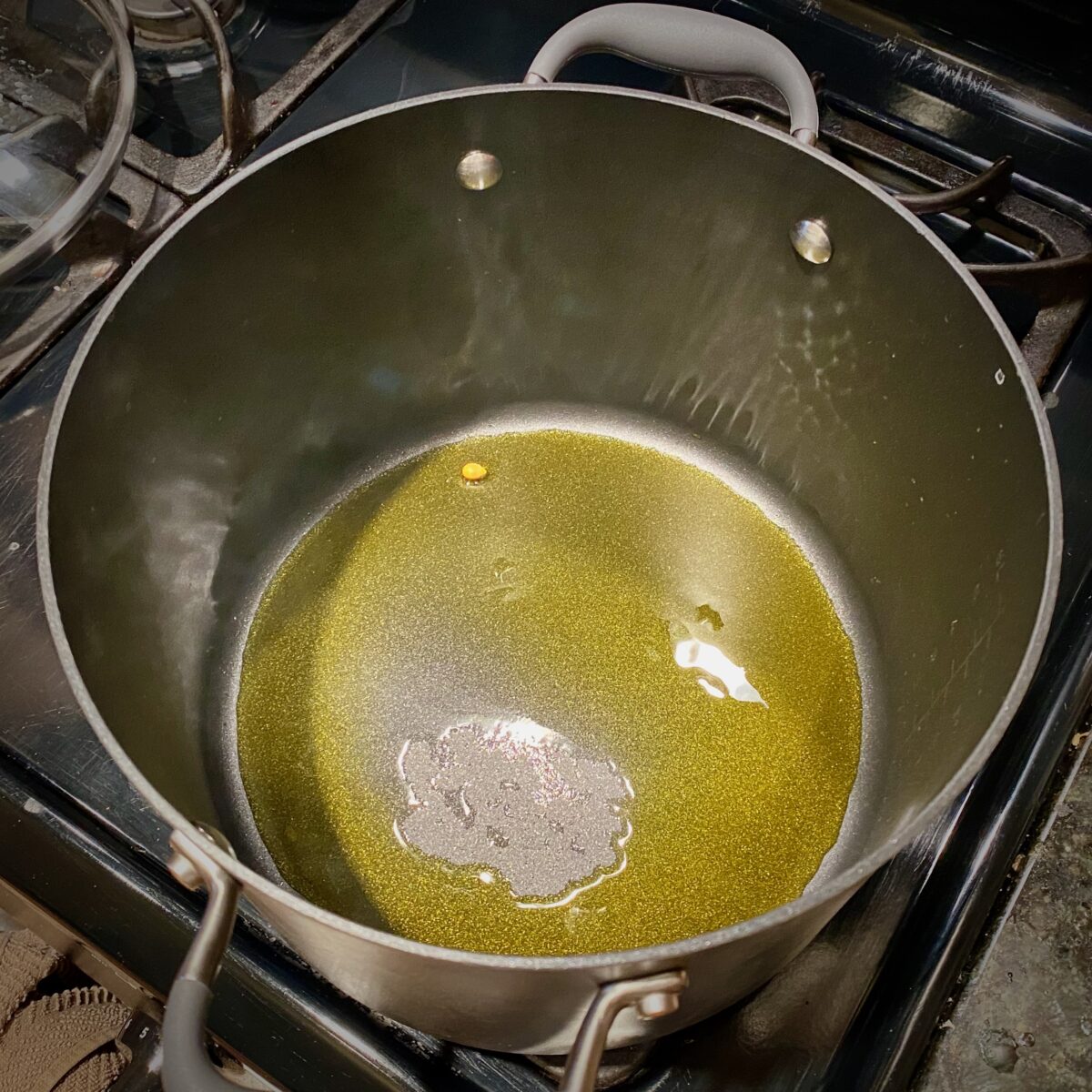 Top view of large pan with hot oil and one kernel of corn in it. The kernel is unpopped and at the far edge of the pan. 