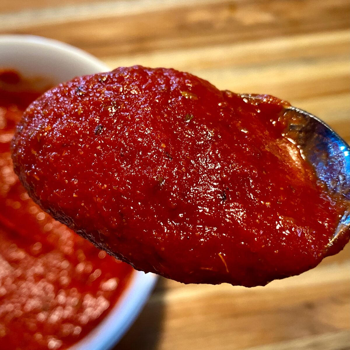 Close up view of zesty pizza sauce on a spoon showing the herbs and spices.