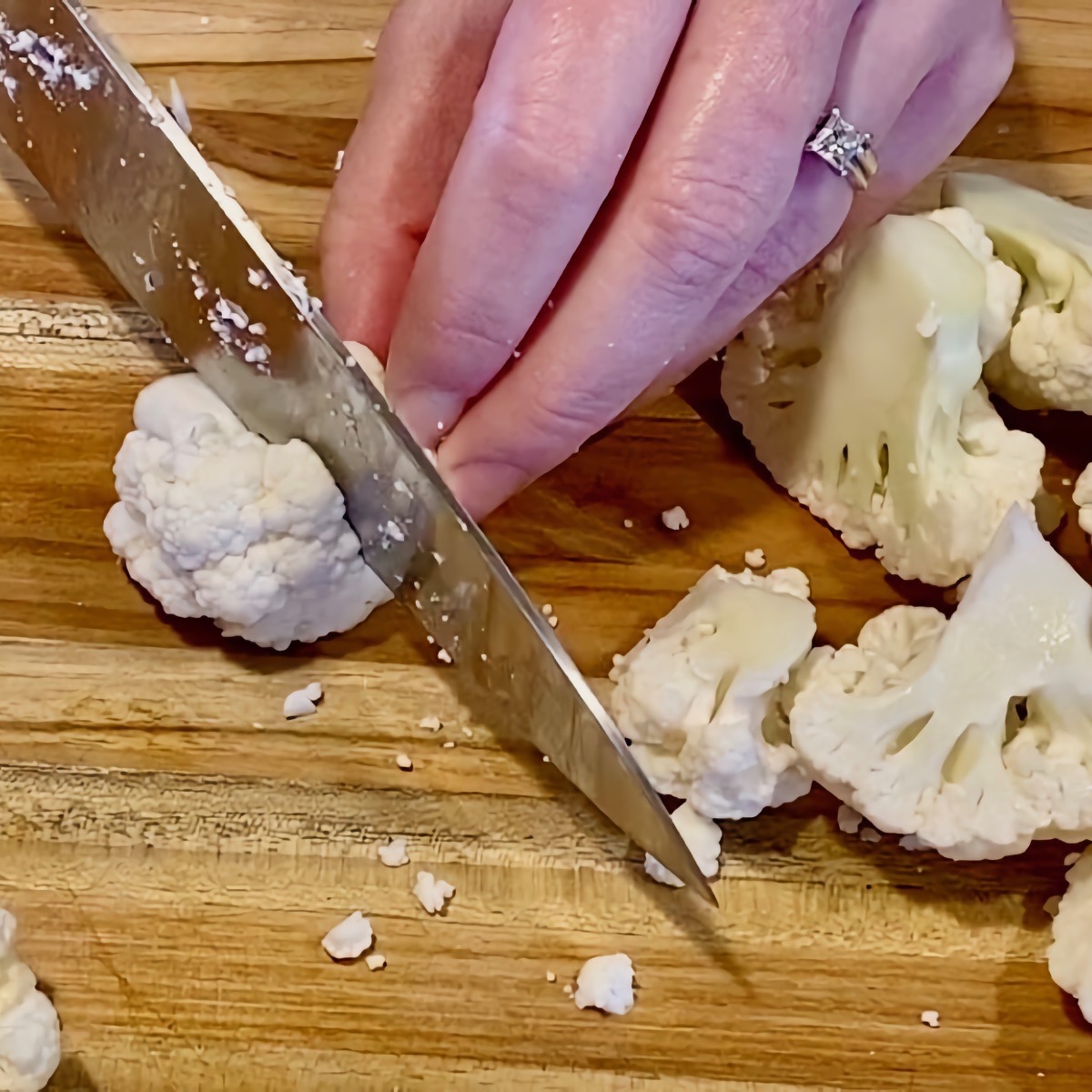 Close up view of a knife cutting cauliflower florets into 1 inch pieces on a cutting board.
