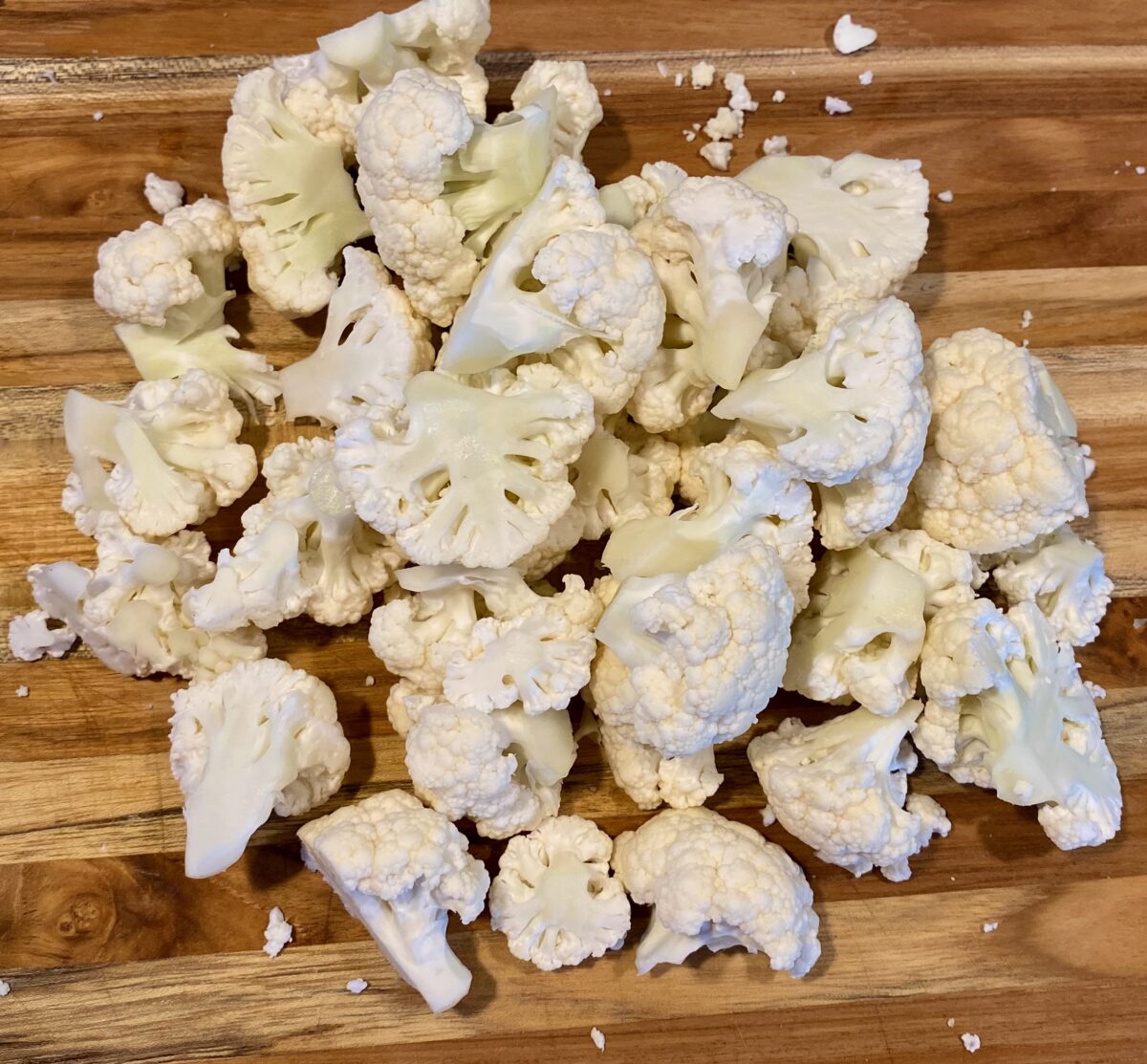 Large pile of trimmed cauliflower pieces on a cutting board ready to be microwaved.