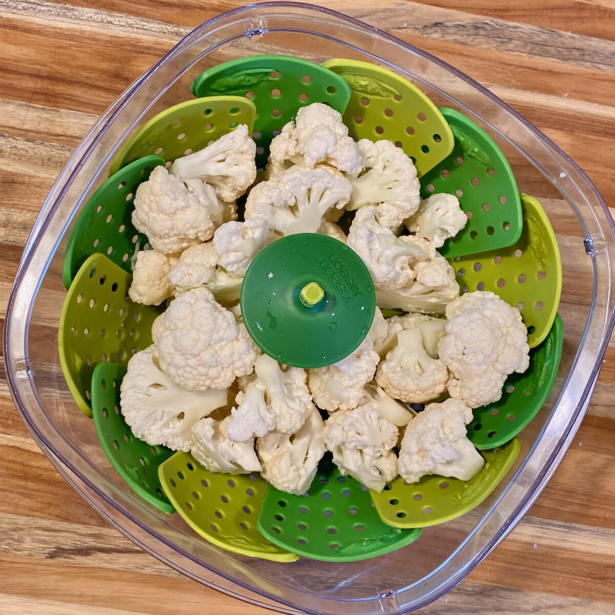 Top view of trimmed cauliflower pieces inside a microwavable steamer.