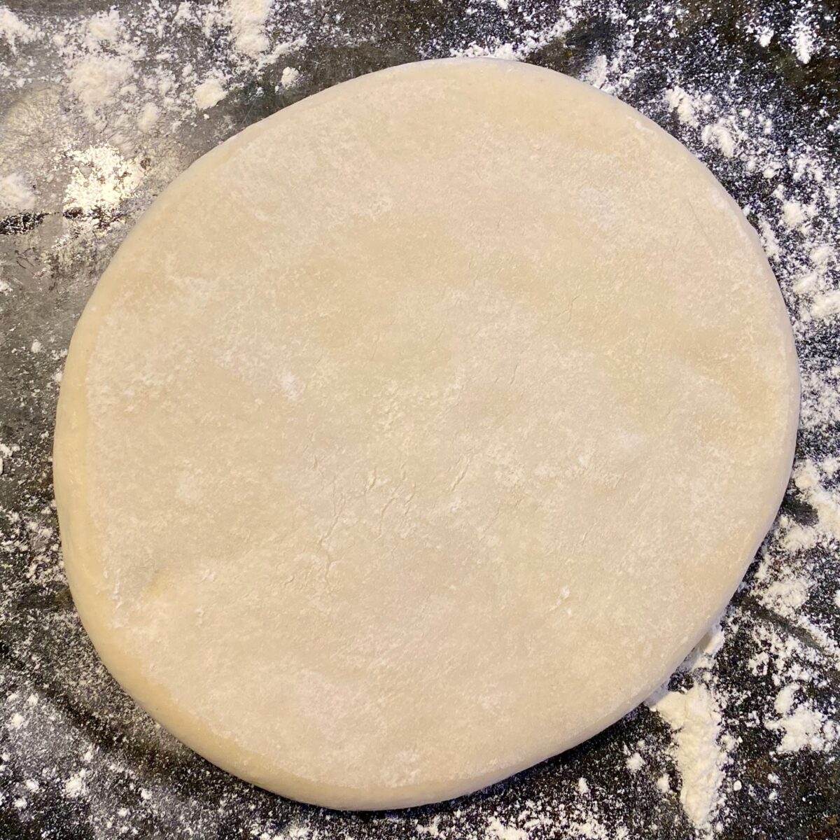 top view of a pizza dough on a floured counter top that still needs to be stretched into a pizza crust.