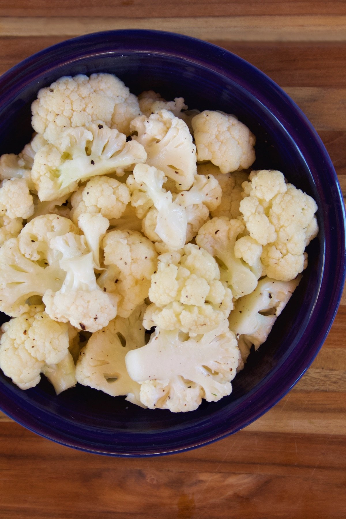 Top view of microwaved cauliflower in a blue bowl on a wooden cutting board.