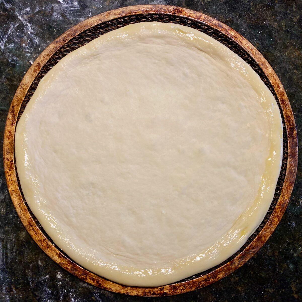 top view of stretched pizza crust that has olive oil applied to the outer edge.