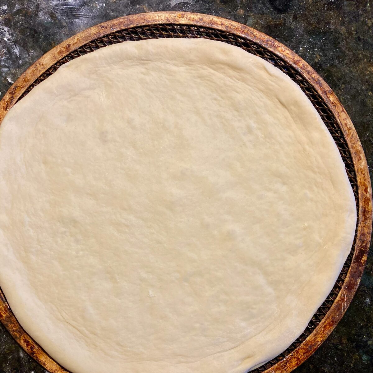 top view of stretched pizza dough on an aluminum pizza screen.