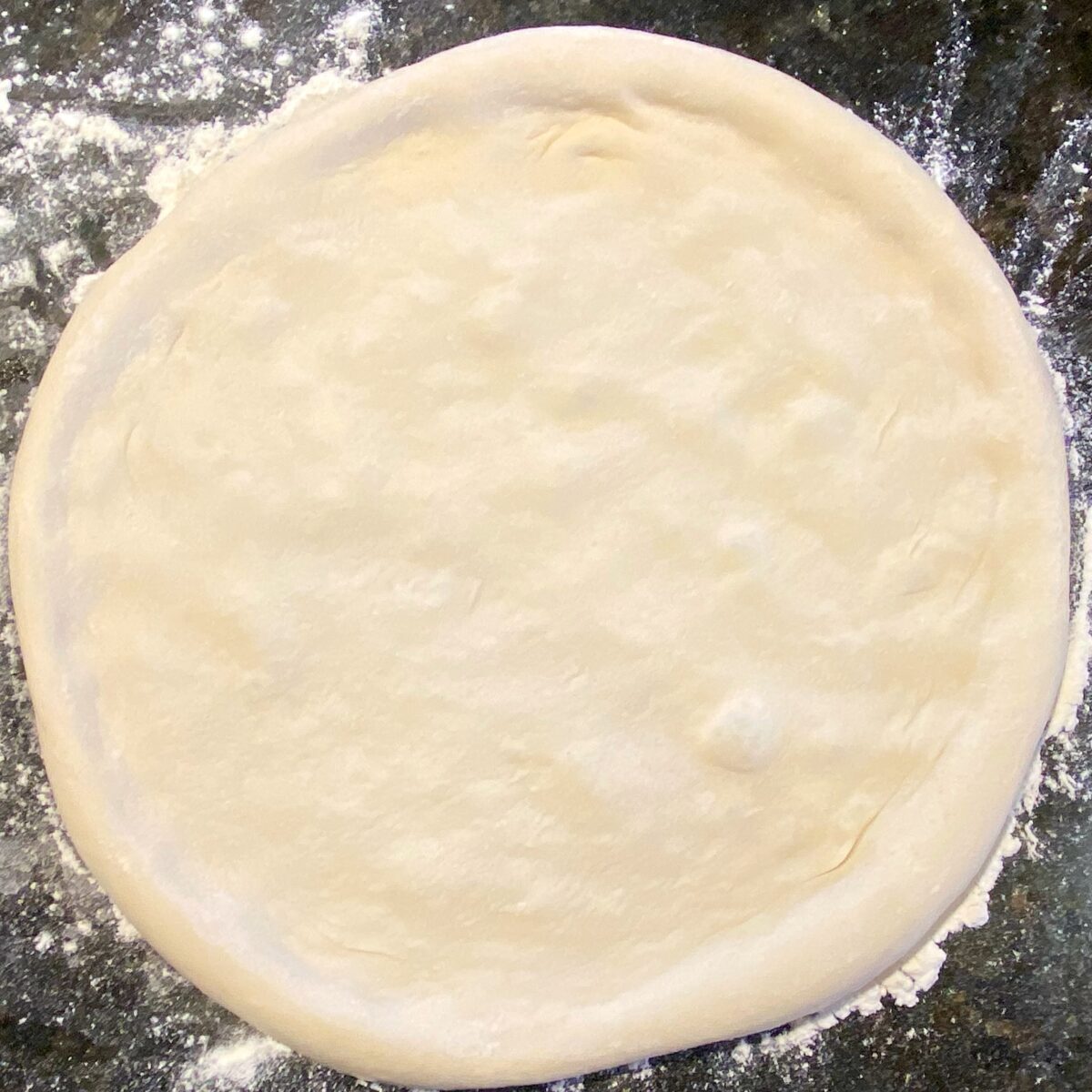 top view of stretched pizza dough showing a bunch of air pockets forming.