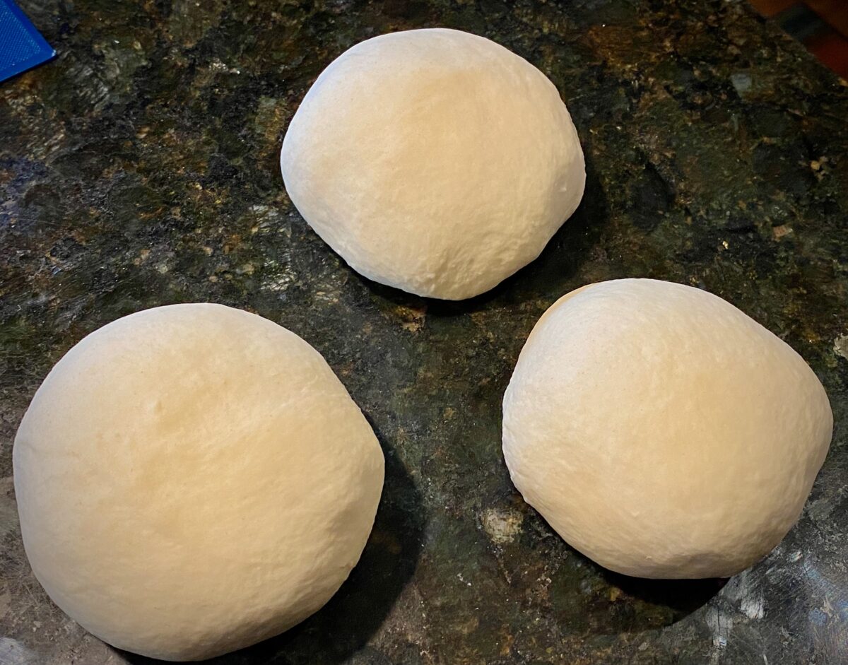 Top view of three formed pizza dough balls on a granite counter top.