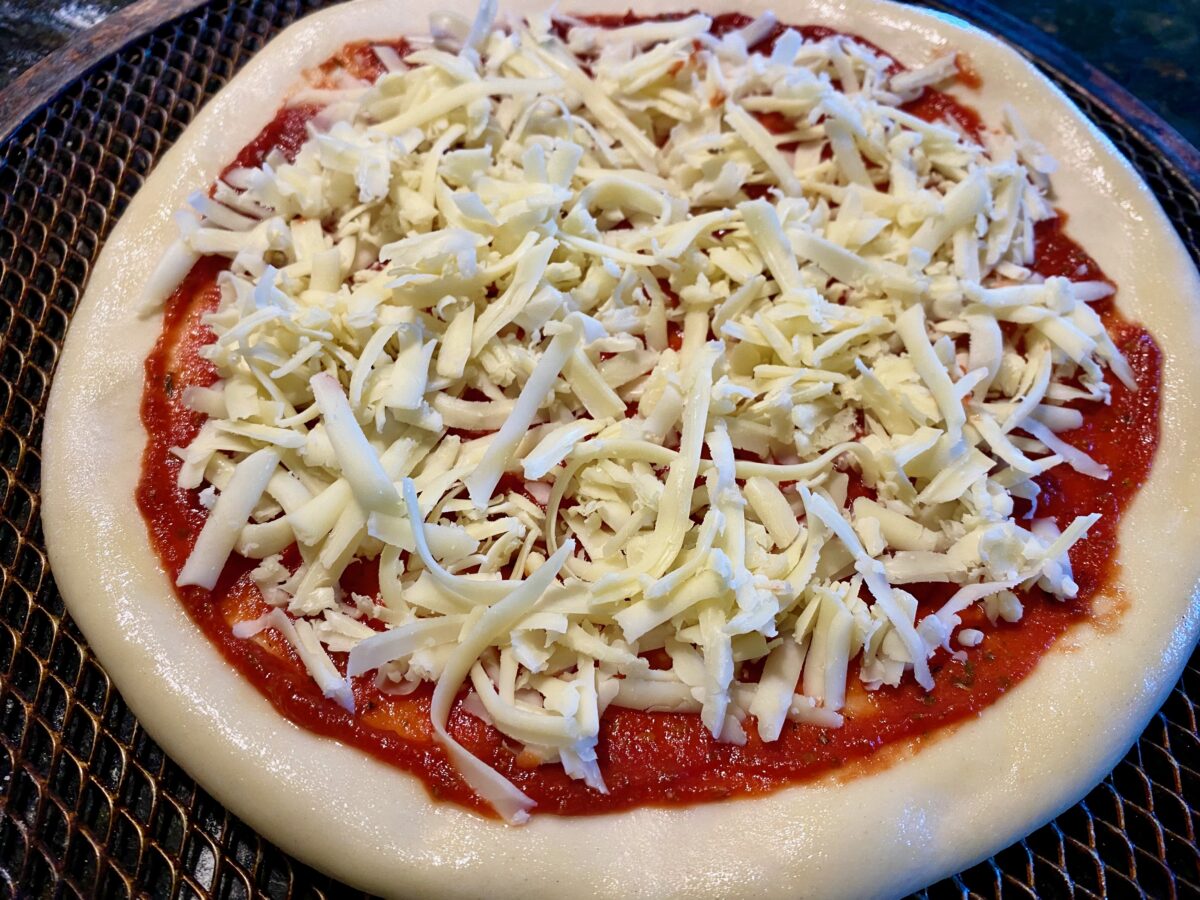 top view of pizza crust just just had shredded cheese applied to it.