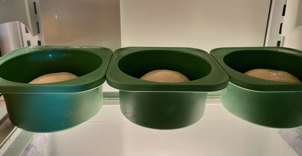 Side view of three uncovered dough balls in oiled containers in the back of my refrigerator.