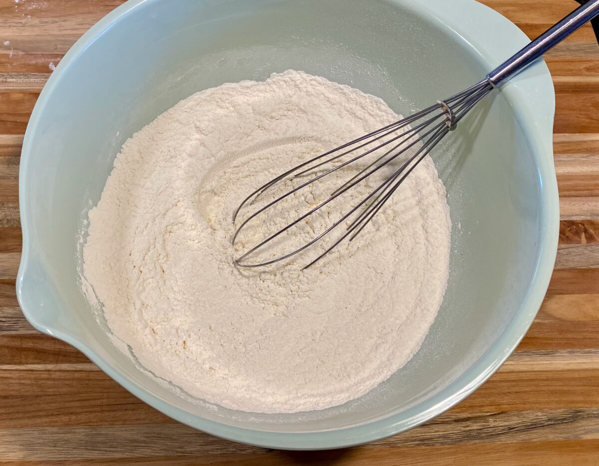 Dry ingredients mixed in a large mixing bowl with a whisk inside of it.