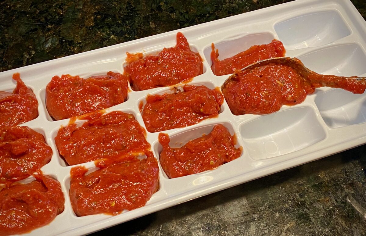 Top view of a spoon loading pizza sauce into an ice cube tray.
