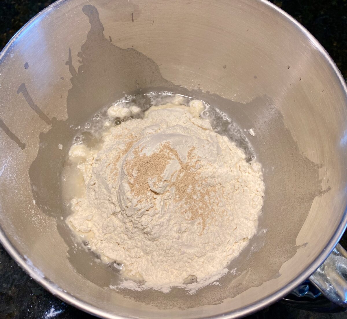 Top view of pizza dough ingredients just added to mixing bowl. They include water, salt, sugar, flour and yeast.