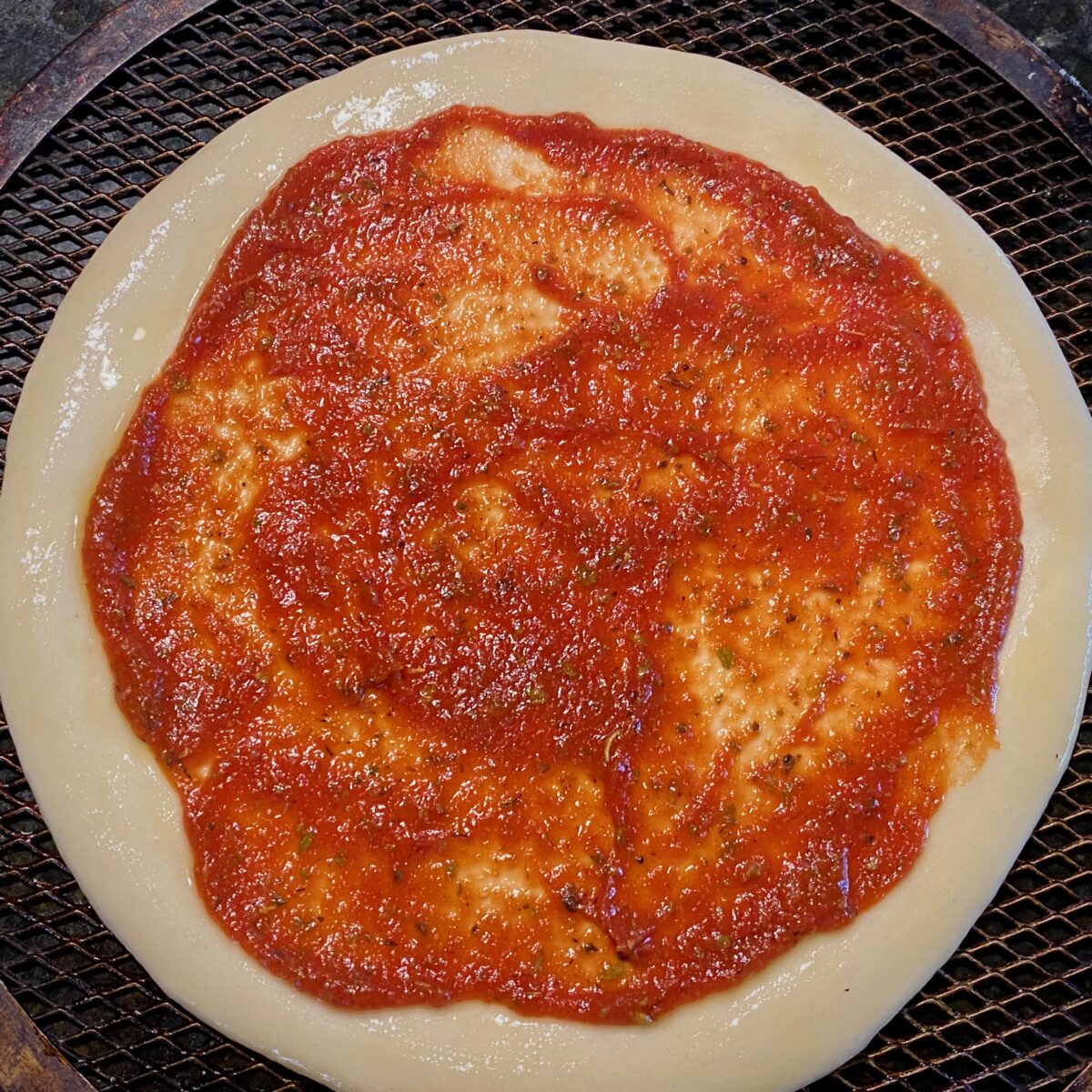 Top view of pizza sauce spread evenly on top of homemade pizza crust.