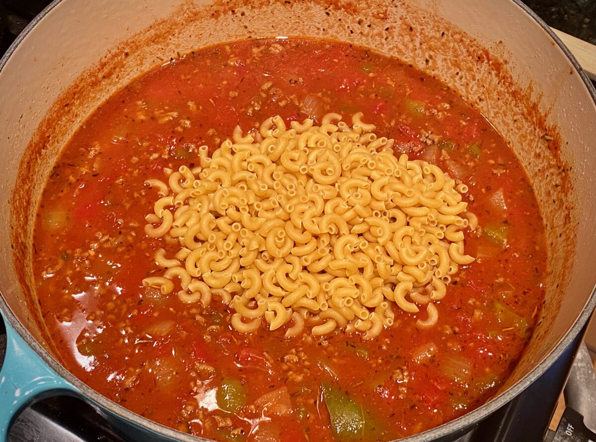 Top view of american goulash where the uncooked noodles have just been added and are resting on the top of the soup.