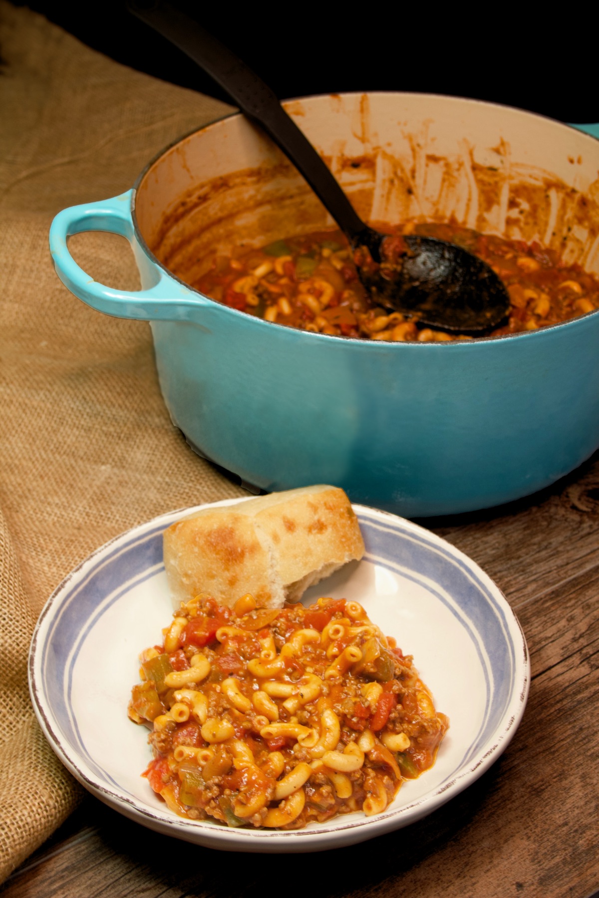 Side view of a bowl of one pot american goulash with a piece of crunch bread along side of it.