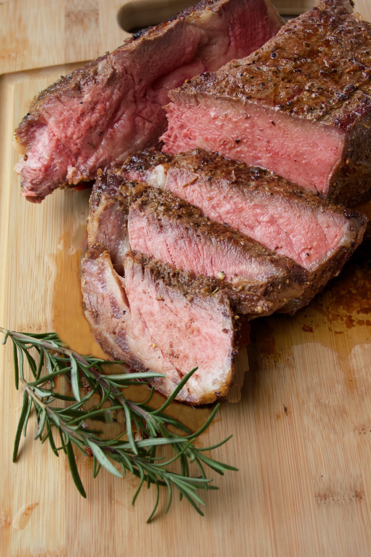 Reverse-Seared Ribeye Steak, freshly sliced on a cutting board with rosemary sprigs nearby.
