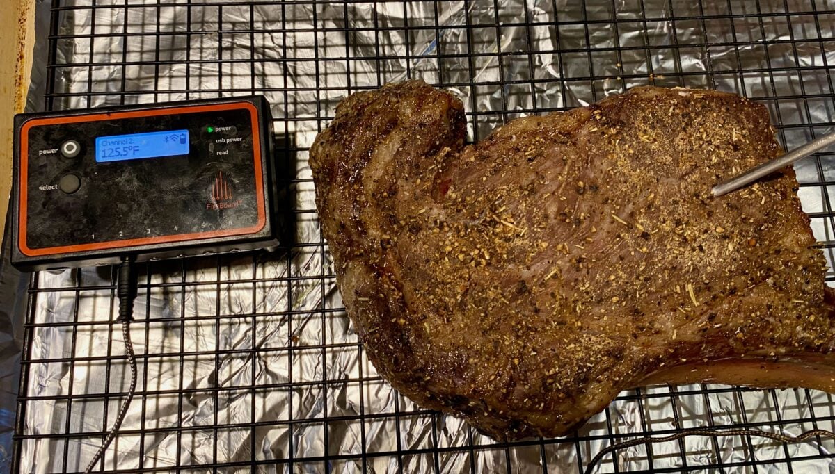 A ribeye on a cooling rack that shows an internal temperature of 125ºF.