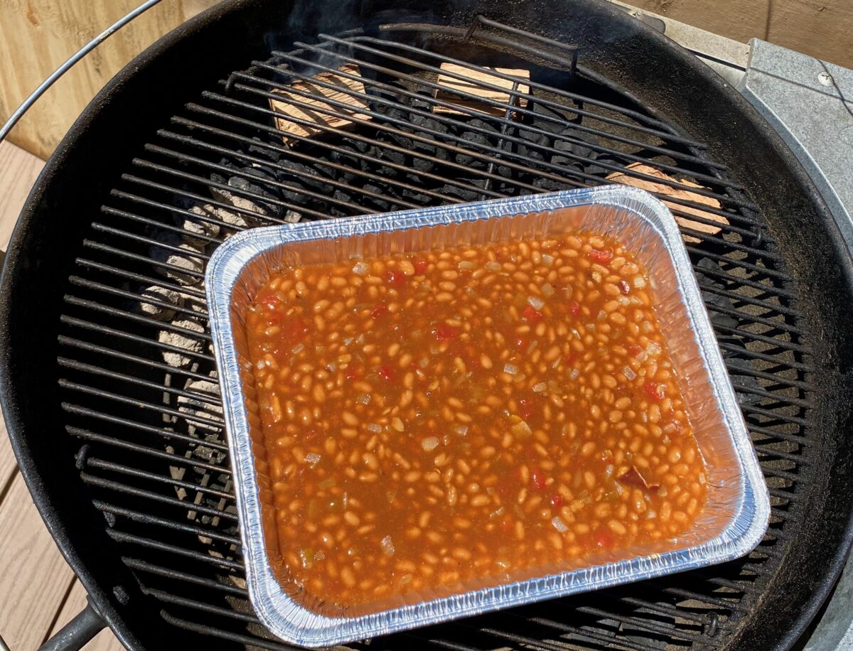 Baked beans placed onto a charcoal grill to be smoked.