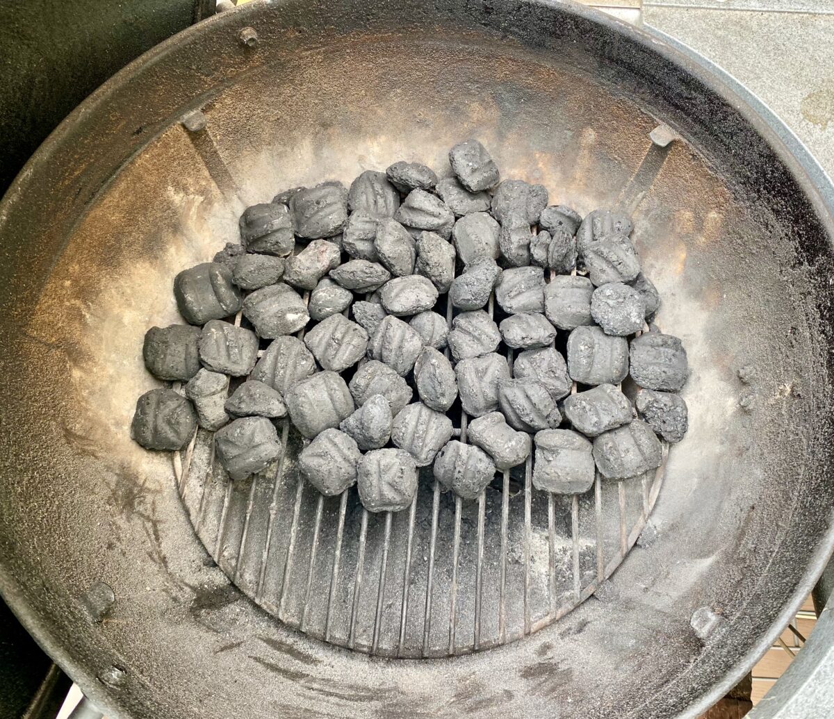 Unlit charcoal covering ⅔ of a kettle grill's cooking area.