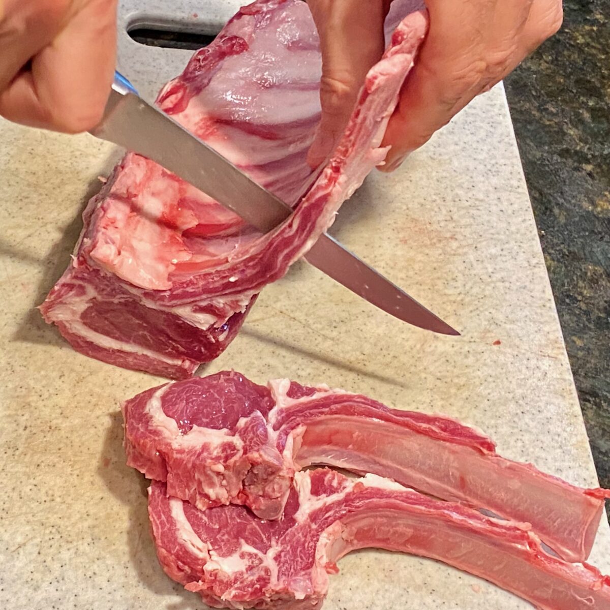 SIde view of a knife slicing off a lamb chop from a rack of lamb.