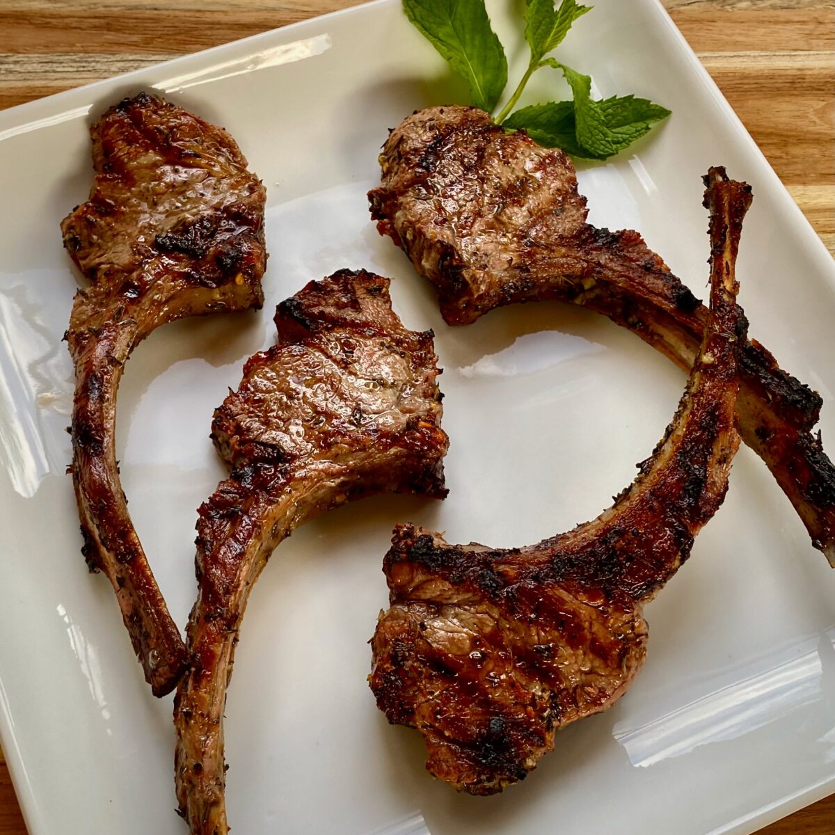 Four greek marinated lamb chops that have been grilled on a square white plate.