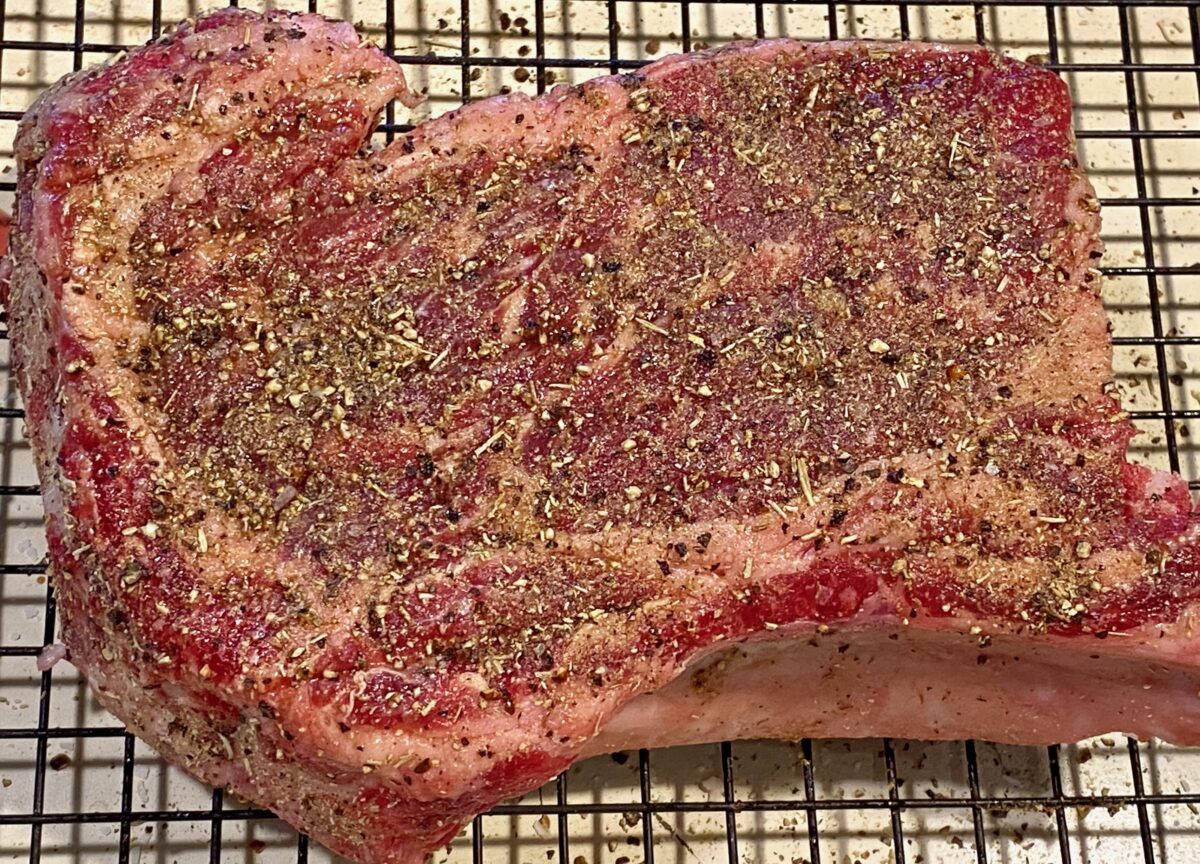 Close up view of a well seasoned raw ribeye on a cooling rack.